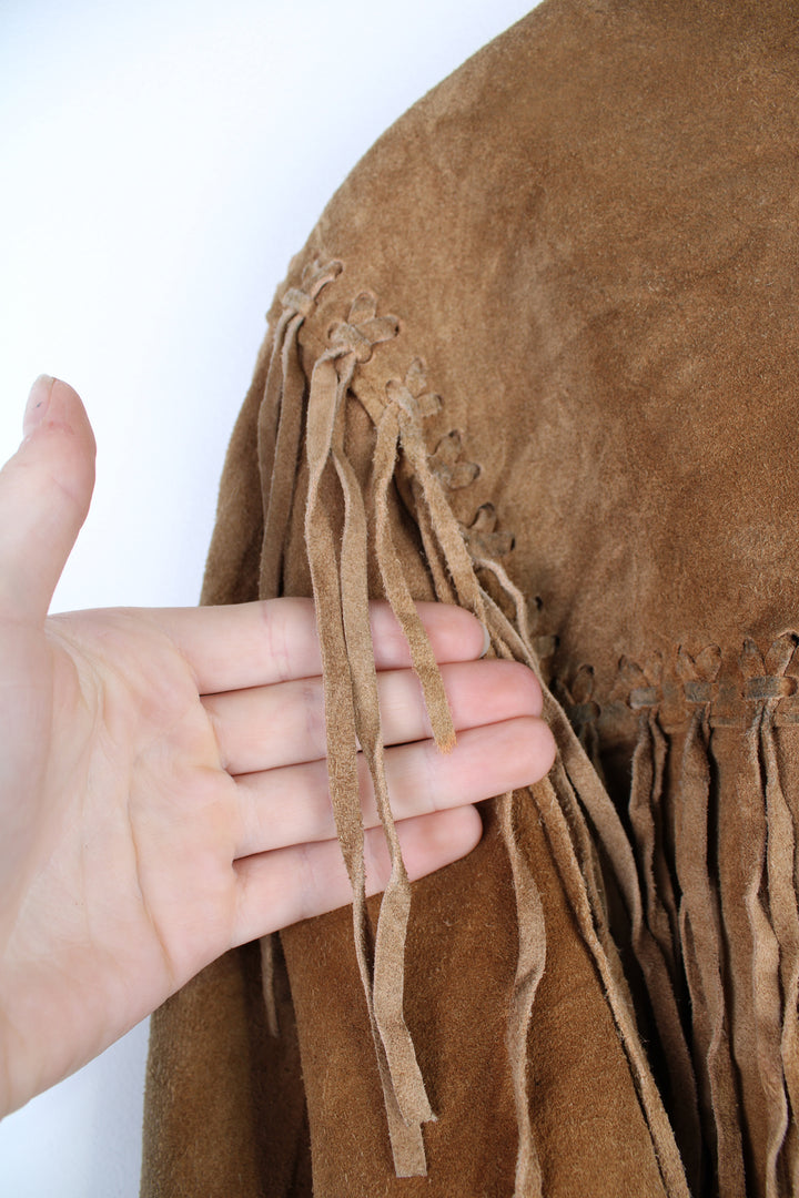 Vintage 90's DKNY fringe jacket. Tan suede jacket with fringe and whip stitch detail. The jacket is fully lined and closes with wooden toggle style buttons down the front. Fair condition - The jacket is discoloured in places and is missing some tassels on the shoulder and pocket. Size in Label: Womens L 12 - 14 