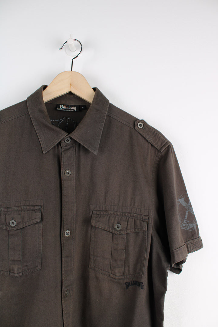 Billabong Short Sleeved Shirt in a khaki and grey colourway, button up, double chest pockets, and has logo embroidered on the front and big back graphic.