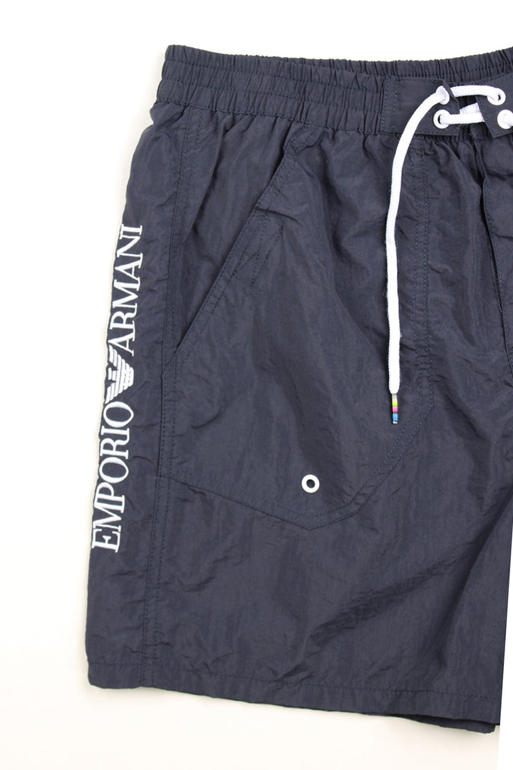 Navy blue Emporio Armani swim shorts with elasticated waistband and lace up tie at the front. Features embroidered logo on the leg.