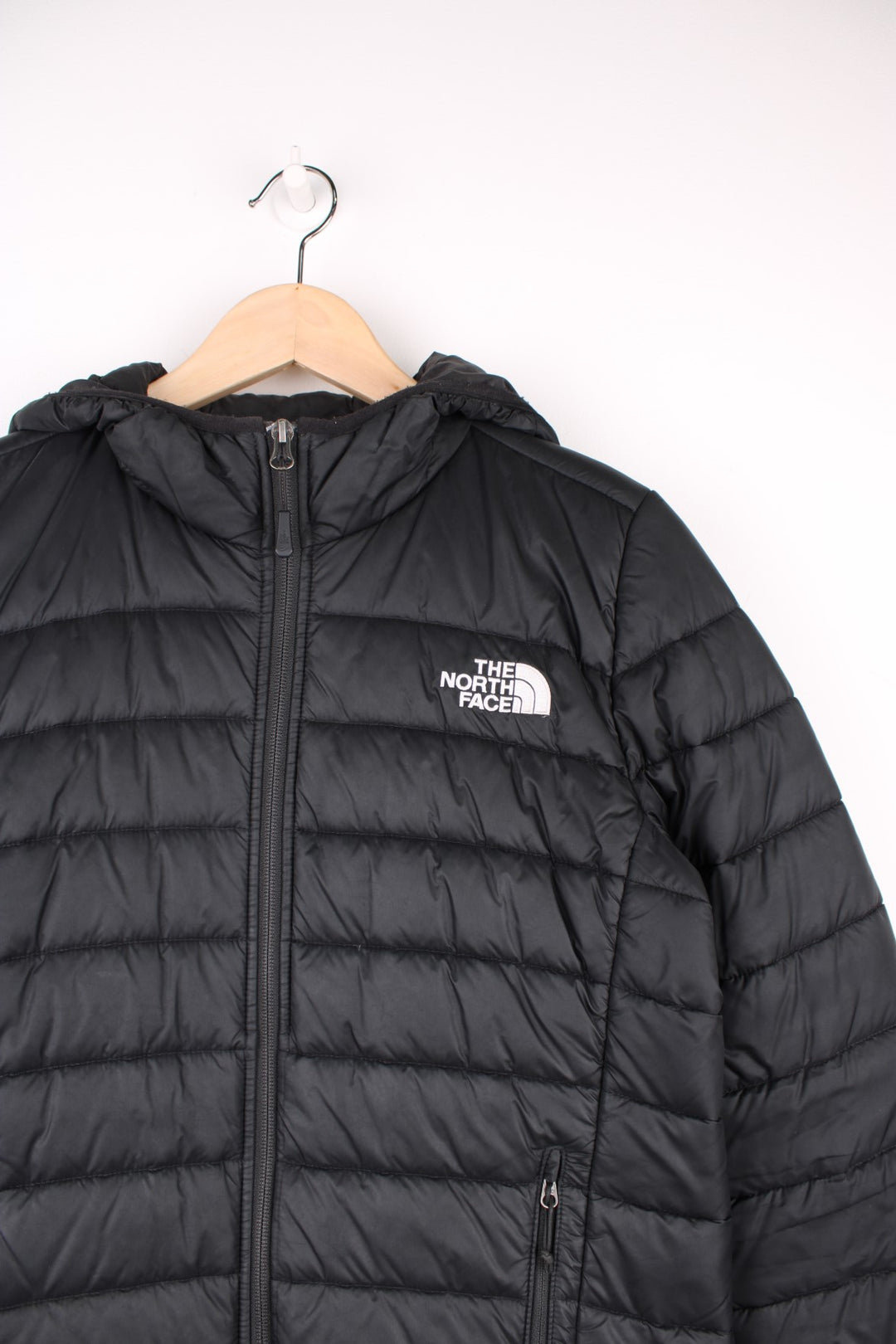 The North Face Puffer Jacket in a black colourway, zip up with side pockets, hooded, insulated, and has the logo embroidered on the front and back.