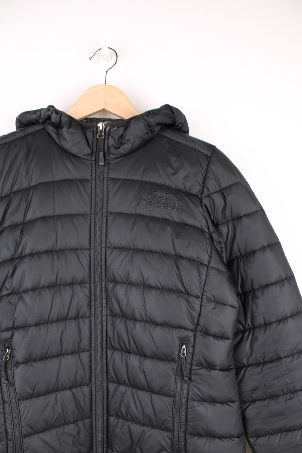 The North Face Puffer Jacket in a black colourway, zip up with side pockets, insulated, hooded, and has the logo embroidered on the front and back.