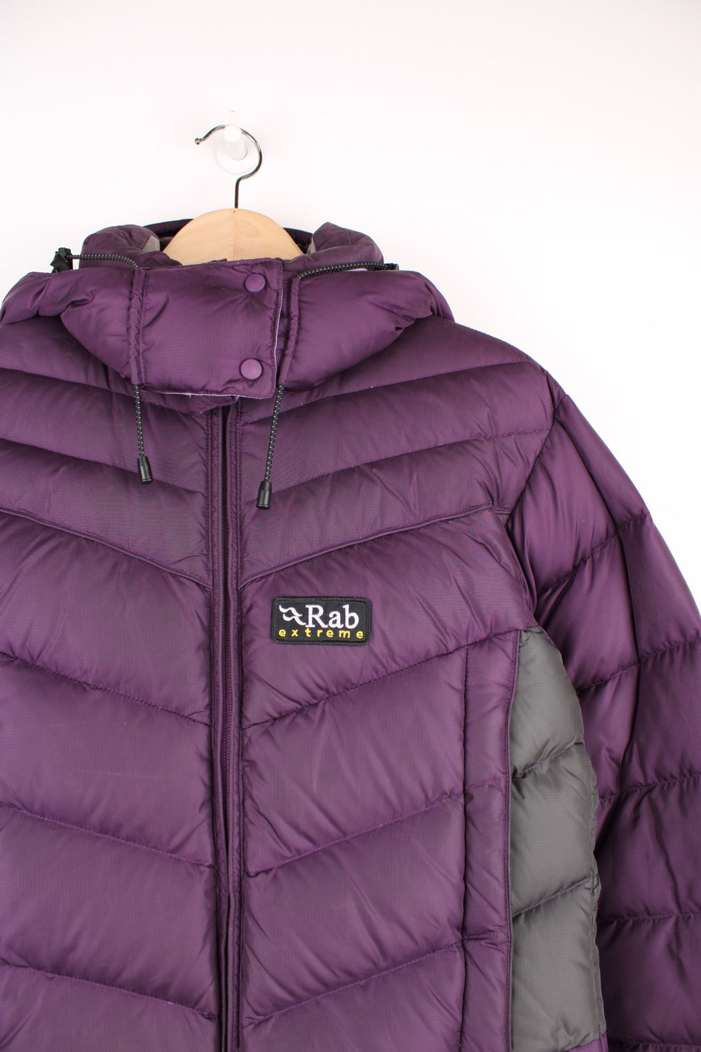 Rab Extreme Puffer Jacket in a purple colourway, zip up with side pockets, has a detachable hood, insulated, and has the logo embroidered on the front.