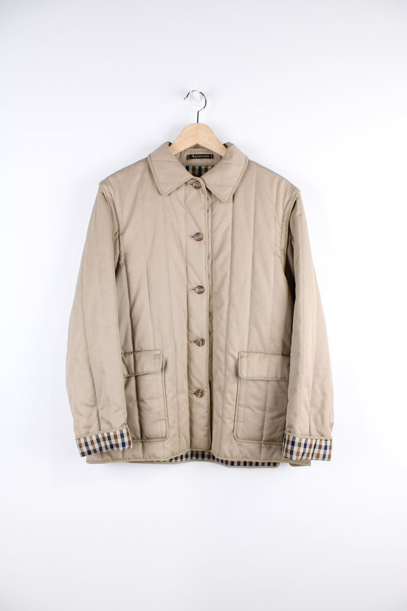 Vintage Aquascutum quilted jacket in a tan colour, button up, has detachable sleeves, two pockets and Aquascutum print lining.