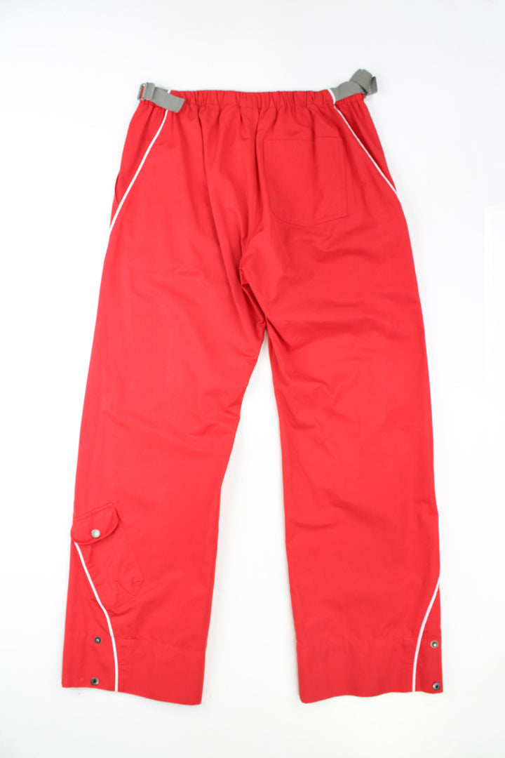 Y2K Nike red tech trouers with embroidered logo on the pocket and elasticated waistband at the back. The trousers also feature buckles at the side of the waistband to adjust the size slightly. They also have popper buttons at the cuffs to taper the leg. Size in Label: Womens L 