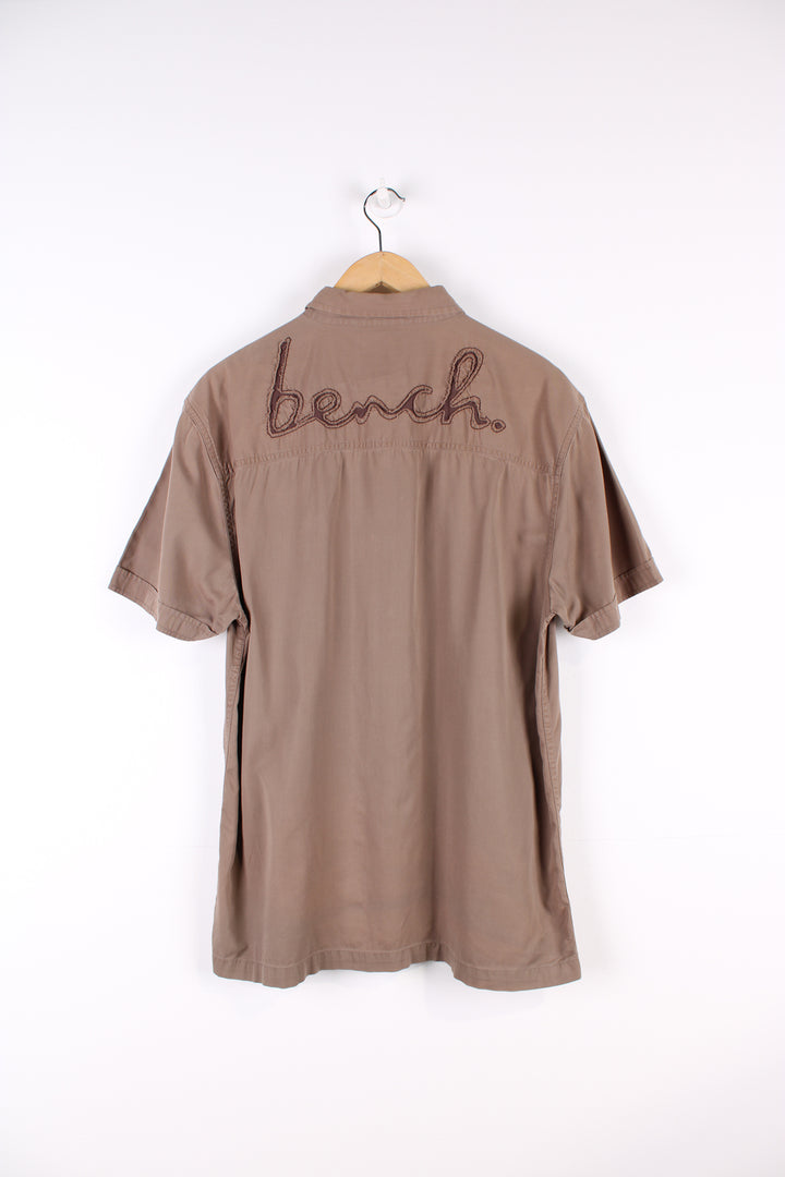 Y2K Bench brown short sleeved, cotton shirt. Features embroidered spell-out logo on the chest and across the back of the shoulders 