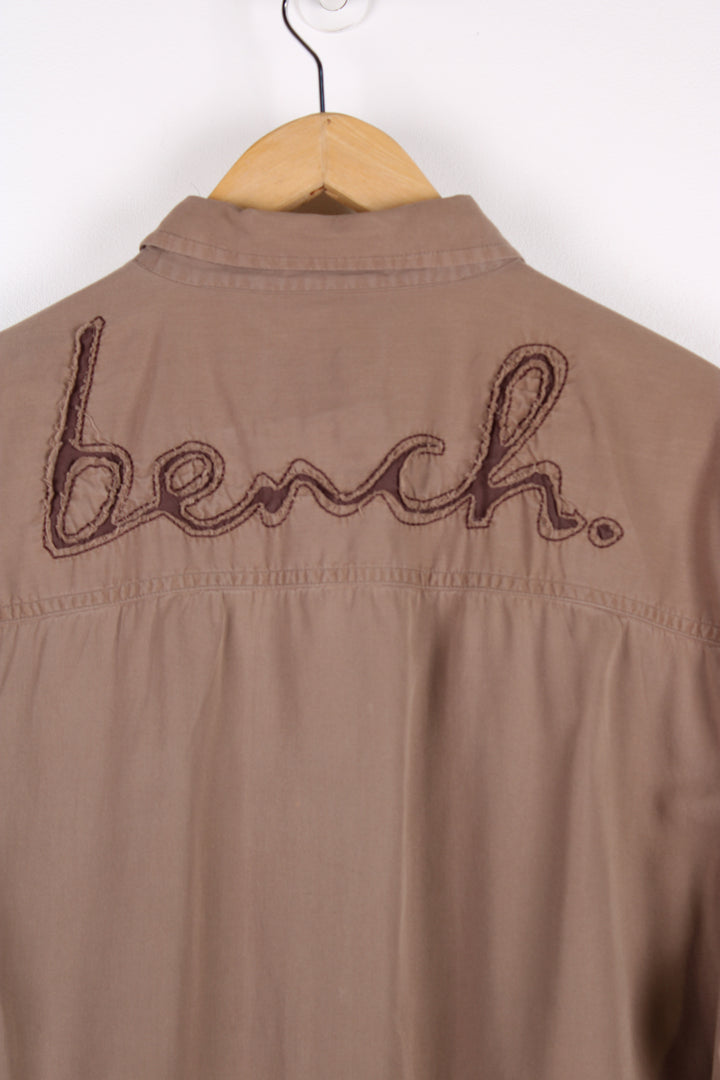 Y2K Bench brown short sleeved, cotton shirt. Features embroidered spell-out logo on the chest and across the back of the shoulders 