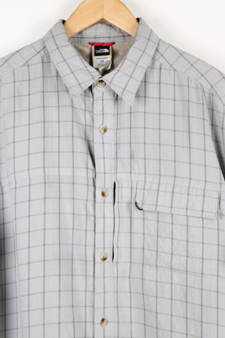 The North Face grey plaid, button up cotton shirt. Features velcro closure chest pocket and spell-out logo on the sleeve