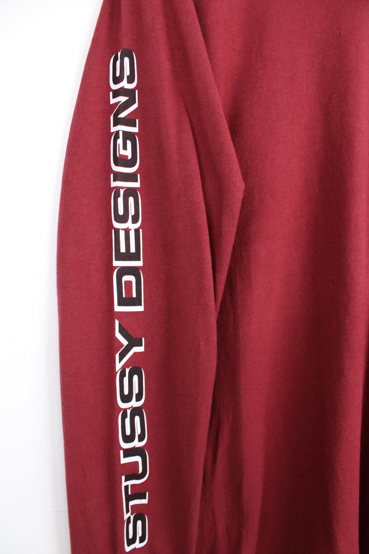 Maroon red Stussy long sleeved t-shirt with yin yang graphic on the front and spell-out graphic down the sleeve 