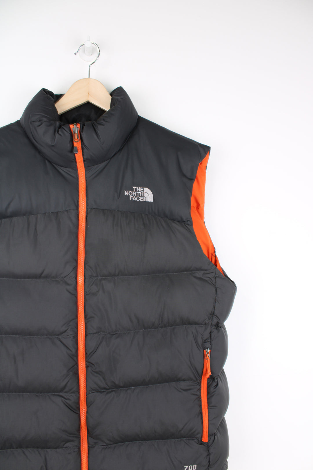 The North Face Face puffer gilet in a grey and orange, zip up with side pockets, insulated and has logo embroidered logo on the front and back.