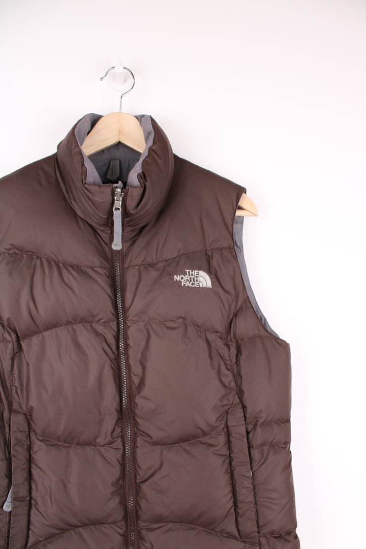 The North Face Face puffer gilet in brown, zip up with side pockets, insulated and has logo embroidered logo on the front and back.