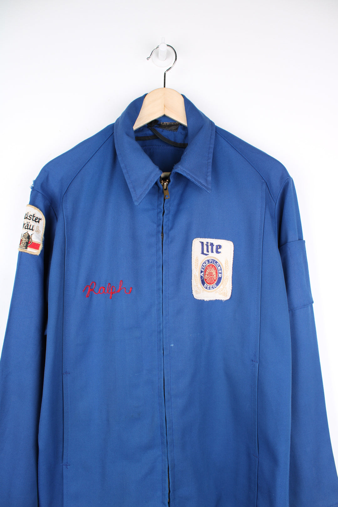 Vintage 1960's delivery drivers jacket from Miller High Life. Features embroidered patches for Miller High Life beer and has chain stitched "Ralph"  on the chest,. Lightweight jacket made from a blue Rayon material, has two front pockets and closes with a full zip. The jacket has a zip inside where it used to have a removable lining (this is missing). 