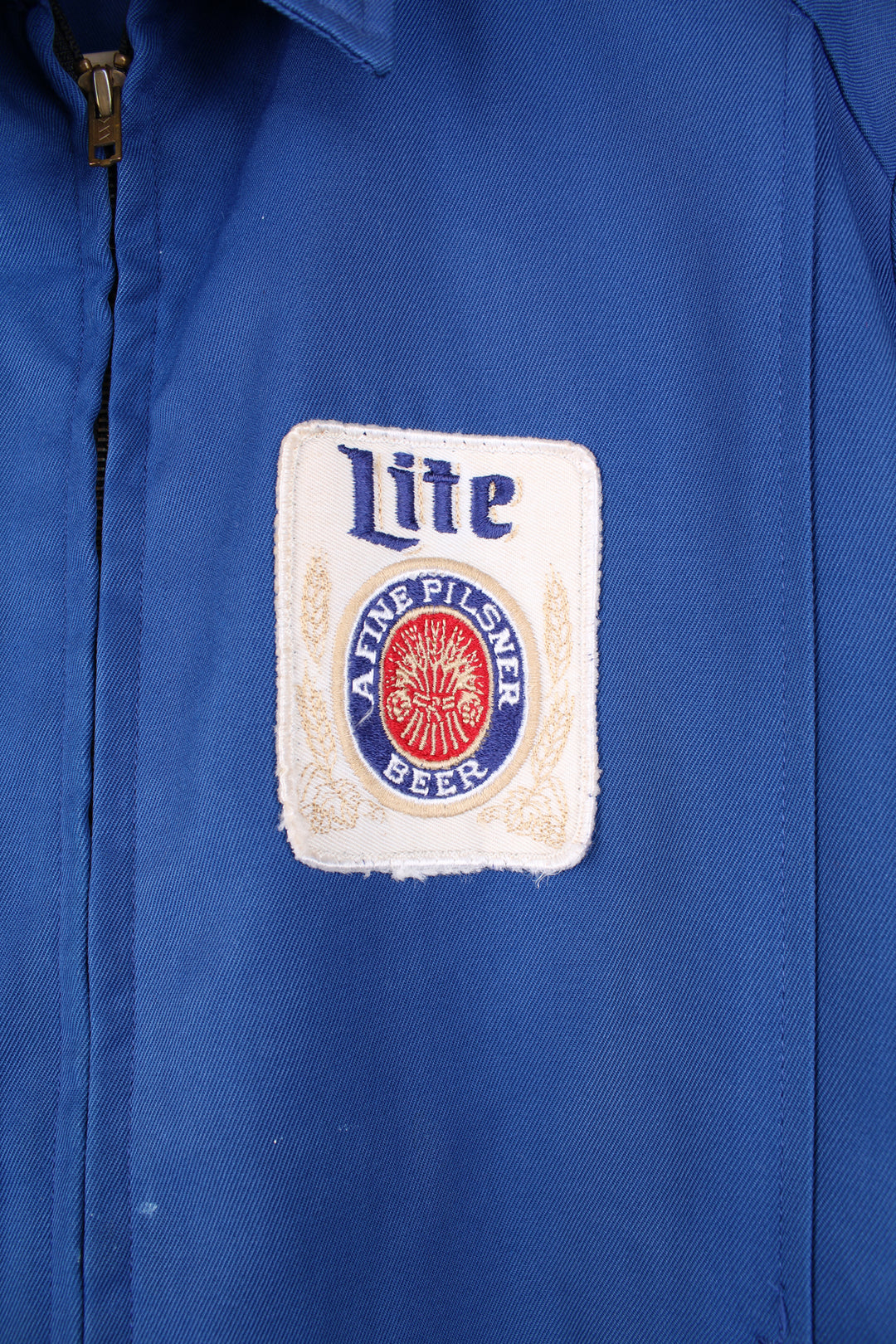 Vintage 1960's delivery drivers jacket from Miller High Life. Features embroidered patches for Miller High Life beer and has chain stitched "Ralph"  on the chest,. Lightweight jacket made from a blue Rayon material, has two front pockets and closes with a full zip. The jacket has a zip inside where it used to have a removable lining (this is missing). 