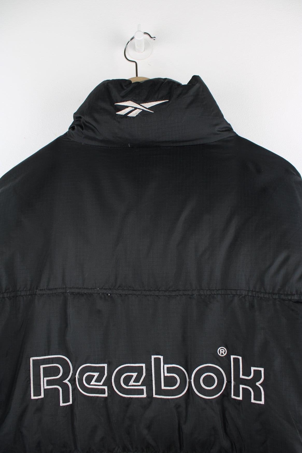 Vintage Reebok puffer jacket in black, zip up, insulated, side pockets and has the logo spell-out embroidered on the front and back.