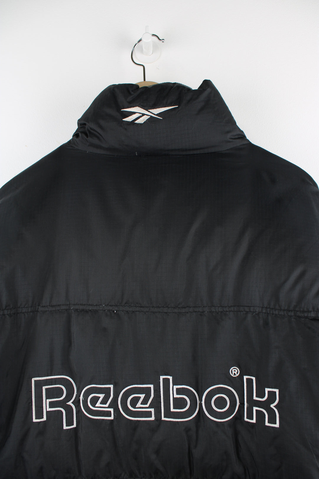 Vintage Reebok puffer jacket in black, zip up, insulated, side pockets and has the logo spell-out embroidered on the front and back.