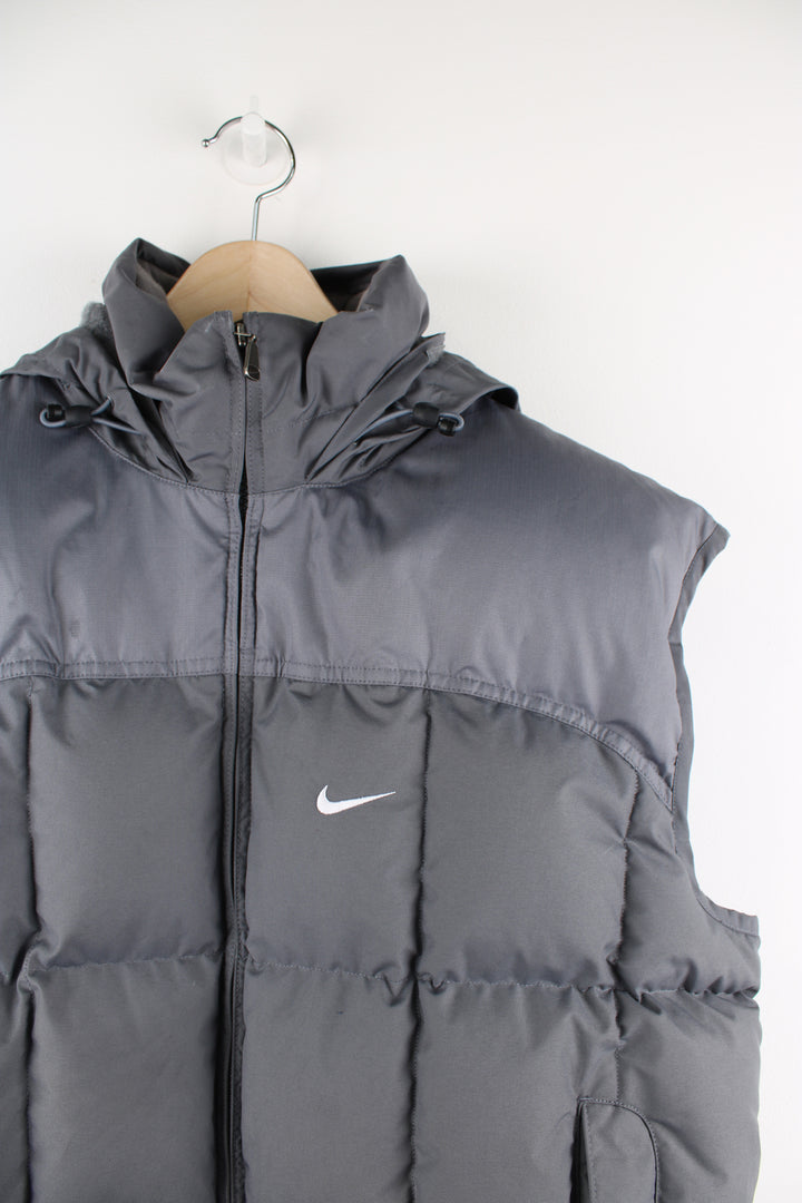 Vintage Nike padded gilet in grey, zip up, insulated, hidden hood, and has swoosh logo embroidered on the front. 