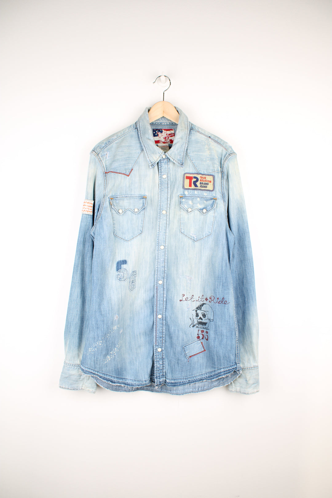 True Religion light wash heavily distressed denim shirt features embroidered badge and printed traditonal tattoo style graphics all over 