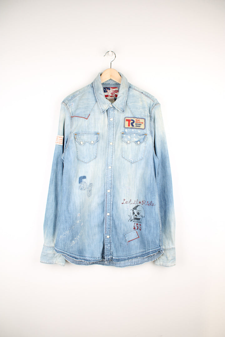 True Religion light wash heavily distressed denim shirt features embroidered badge and printed traditonal tattoo style graphics all over 