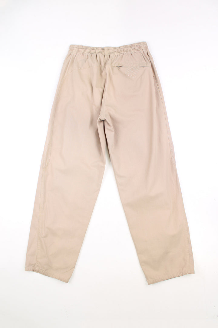 Billabong tan cotton trousers, with high waist and cargo style pockets. Features embroidered logo on the leg 