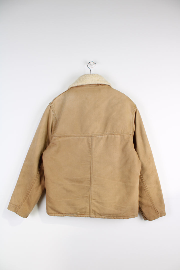 Vintage Carhartt Sherpa Workwear Jacket, in a tan colourway, sherpa lining and collar, multiple pockets, and has embroidered Carhartt logo on the front.