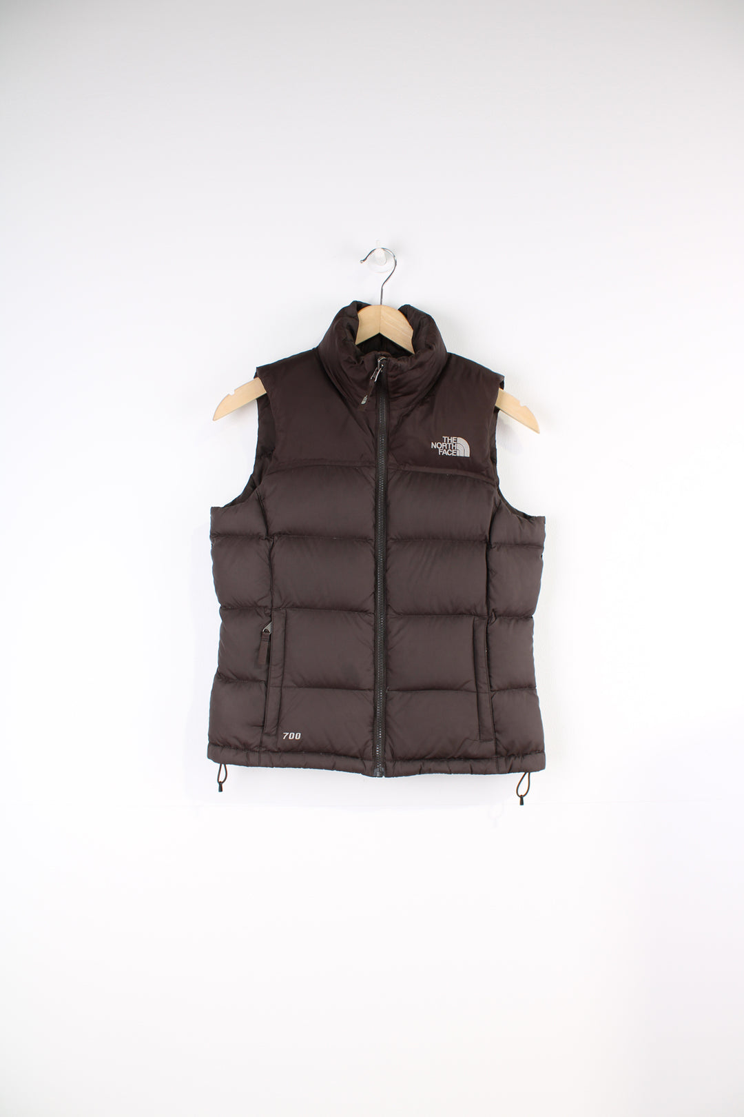 The North Face Face puffer gilet in brown, zip up with side pockets, insulated and has logo embroidered logo on the front and back.