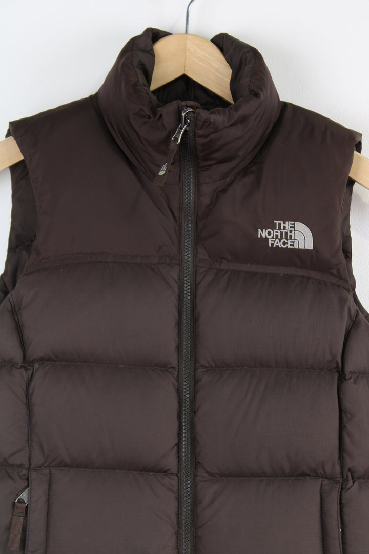 The North Face Face puffer gilet in brown, zip up with side pockets, insulated and has logo embroidered logo on the front and back.