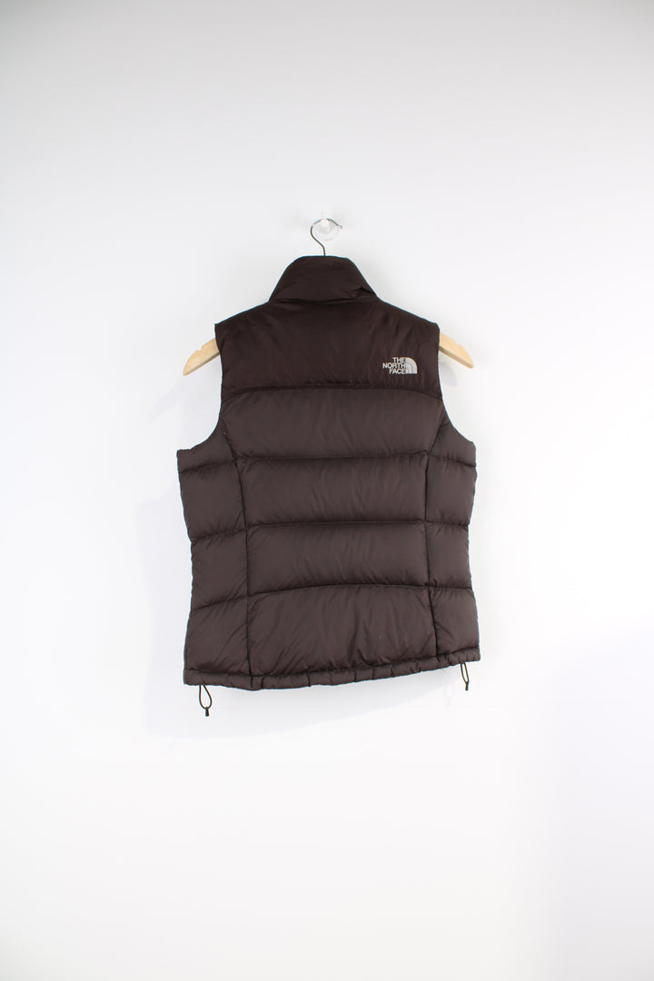 The North Face Face puffer gilet in brown, zip up with side pockets, insulated and has logo embroidered logo on the front and back.