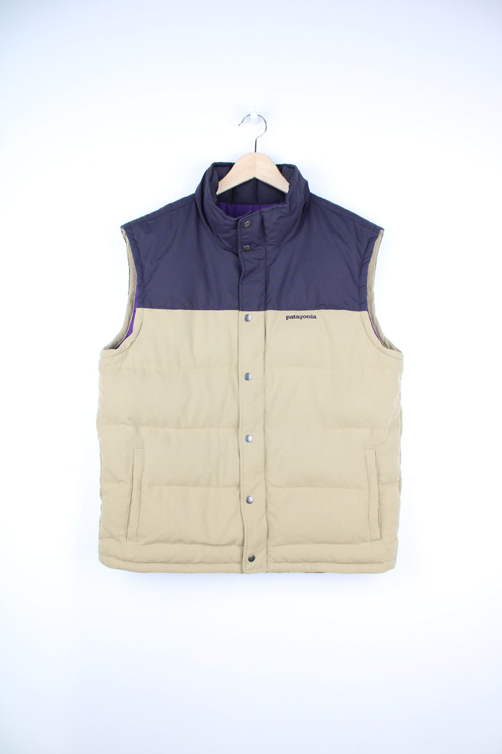 Patagonia Gilet in a tan and dark purple colourway, zip up, side pockets, insulated lining, and has the logo embroidered on the front.