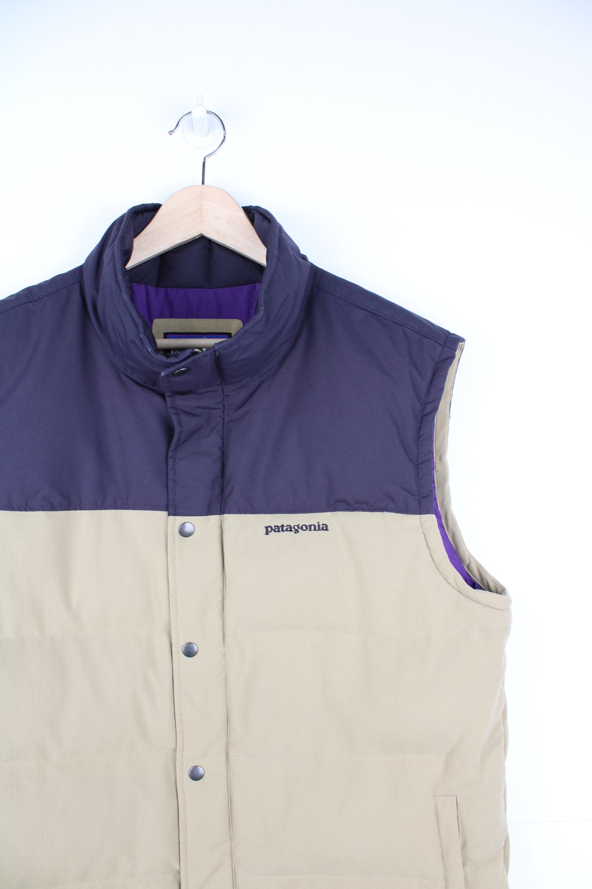 Patagonia Gilet in a tan and dark purple colourway, zip up, side pockets, insulated lining, and has the logo embroidered on the front.