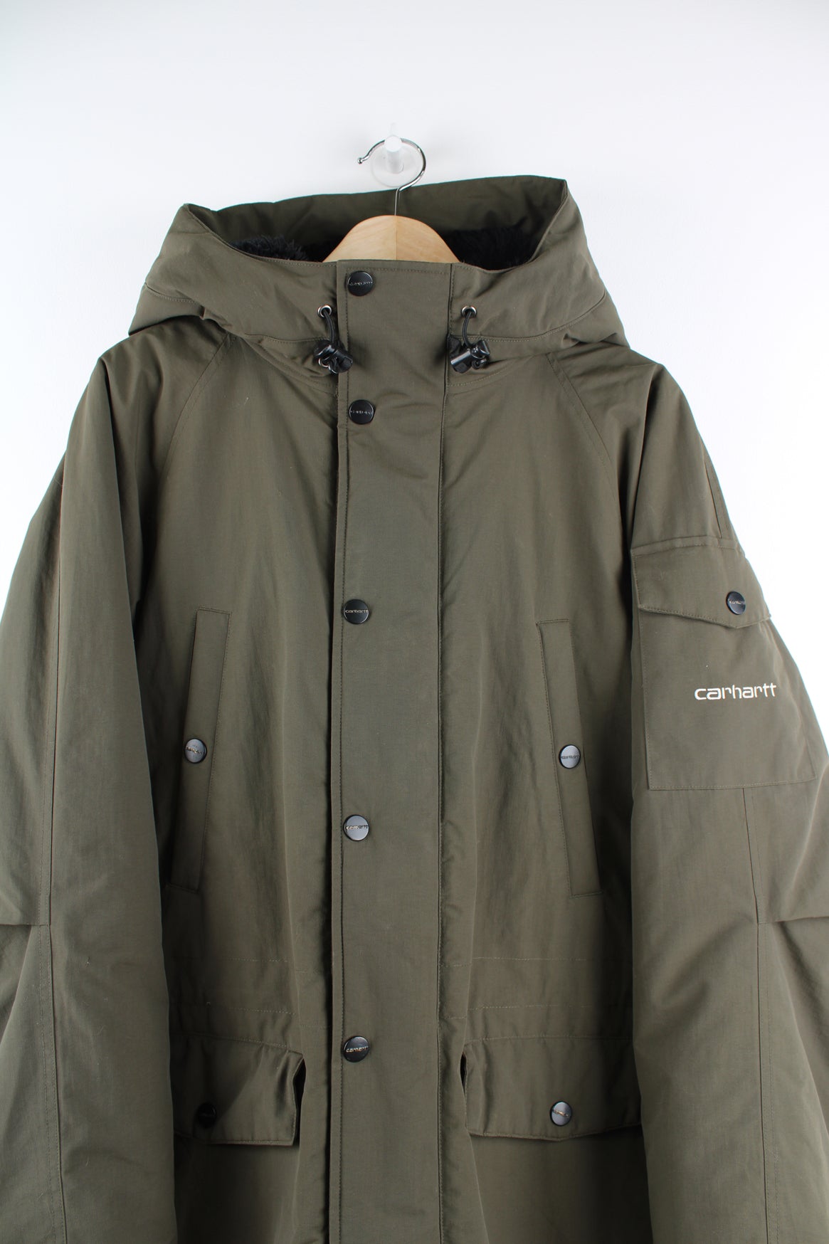 Carhartt Parka Jacket in a green colourway, multiple pockets, hooded with a faux fur lining, zip up, insulated quilted lining, and has the logo embroidered on the front and on the left sleeve.