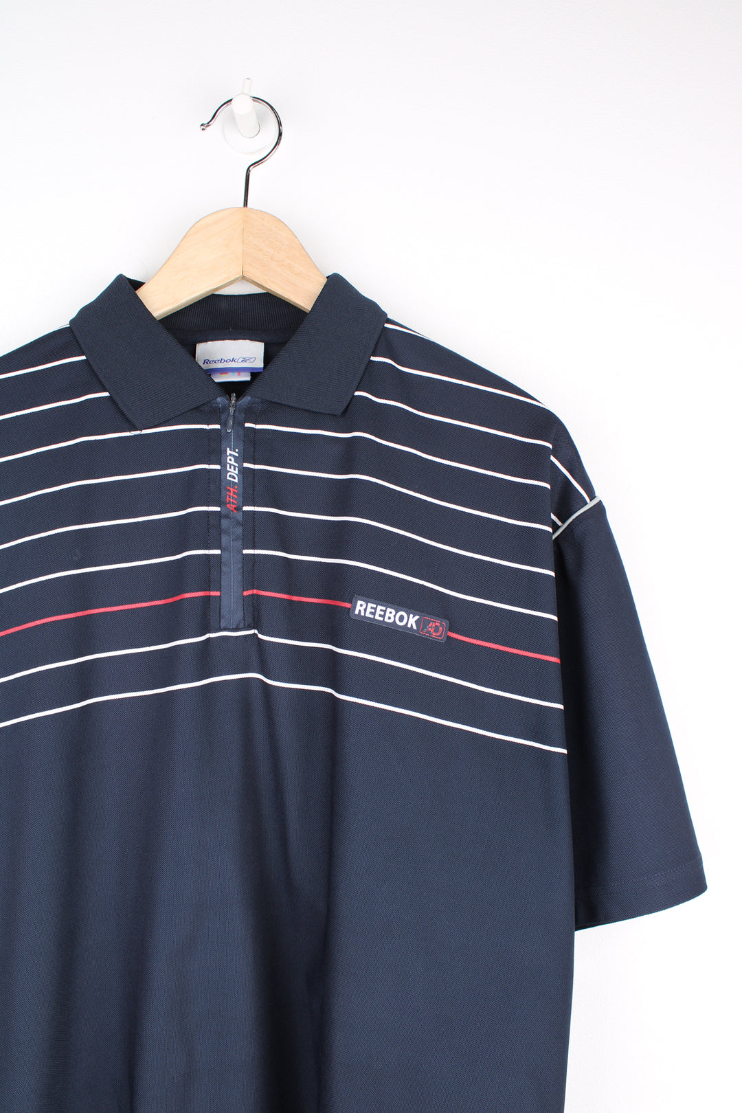 Reebok Athletic Polo Shirt in a navy blue colourway with white and red stripes going across the chest, zip up collar, short sleeved and has the logo spell out embroidered on the front.