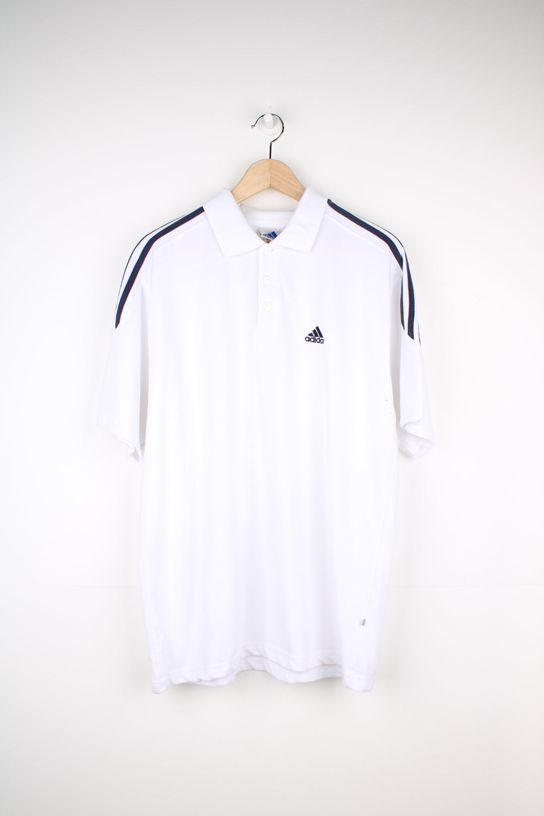 Adidas Polo Shirt in a white and navy colourway with the three stripes going around the shoulders, button up collar, short sleeved and has the logo embroidered on the front.