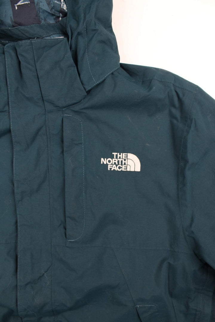 The North Face 2 in 1 Dryvent Jacket in a blue colourway. Zips up and has multiple pockets, detachable gilet lining, hooded, and has the logo embroidered on the front and back.