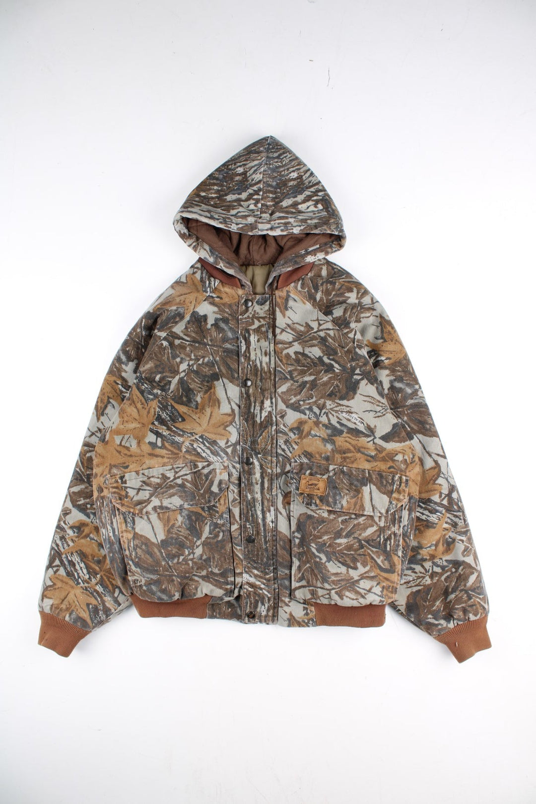 Vintage 90's Duxbak Real Tree Camo Jacket in a brown and green patterned colourway. Zips and buttons up, has multiple pockets, insulated with a quilted lining, hooded, and has the logo embroidered on the front.