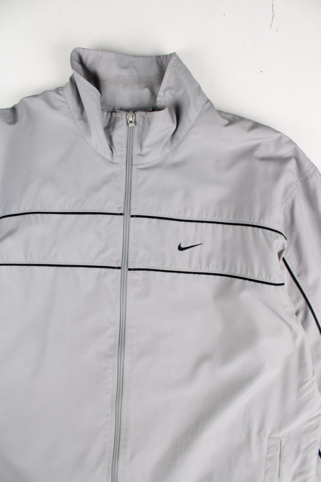 Y2K Nike Tracksuit Jacket in a grey colourway. Zips up and has side pockets, mesh lining, and has the swoosh logo embroidered on the front and back.