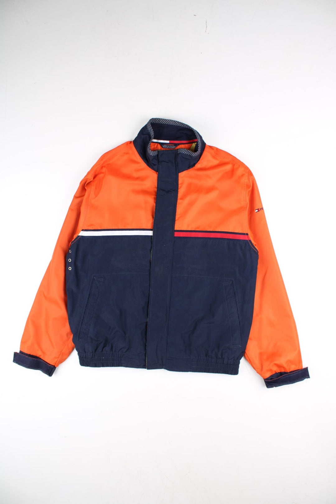 Vintage Tommy Hilfiger Windbreaker Jacket in a orange and blue colourway. Zips up and has side pockets, mesh lining, has the logo stripe going across the front and back, and the spell out embroidered on the left sleeve.