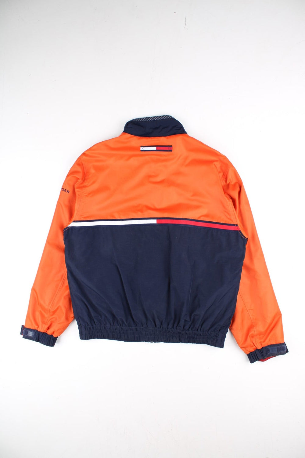 Vintage Tommy Hilfiger Windbreaker Jacket in a orange and blue colourway. Zips up and has side pockets, mesh lining, has the logo stripe going across the front and back, and the spell out embroidered on the left sleeve.