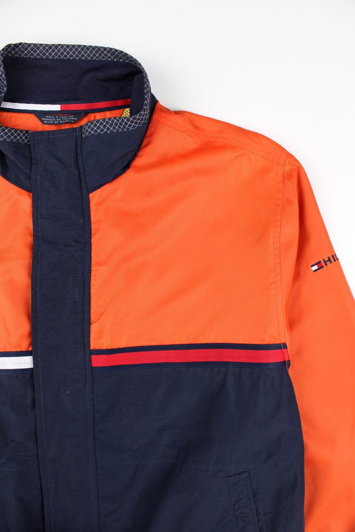 Vintage Tommy Hilfiger Windbreaker Jacket in a orange and blue colourway. Zips up and has side pockets, mesh lining, has the logo stripe going across the front and back, and the spell out embroidered on the left sleeve.