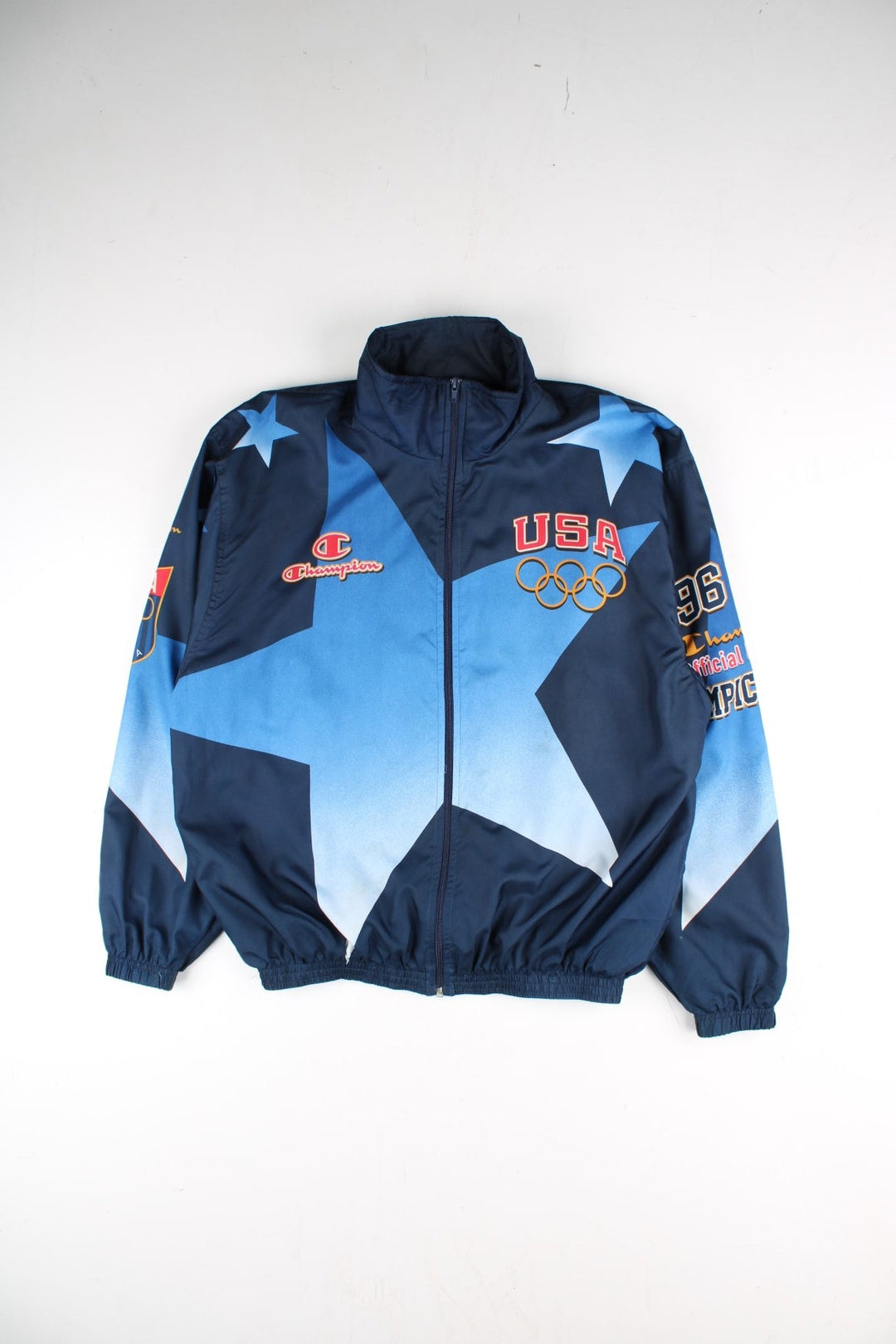 Vintage 1996 Champion USA Olympic Team Track Jacket in a blue colourway. Zips up and has side pockets, and the logos printed on the front, back and on the sleeves.