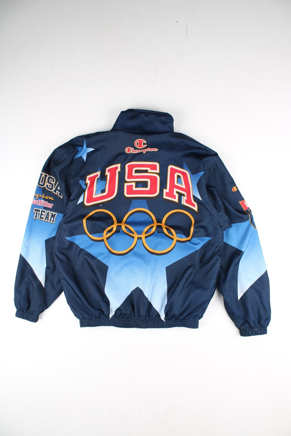 Vintage 1996 Champion USA Olympic Team Track Jacket in a blue colourway. Zips up and has side pockets, and the logos printed on the front, back and on the sleeves.