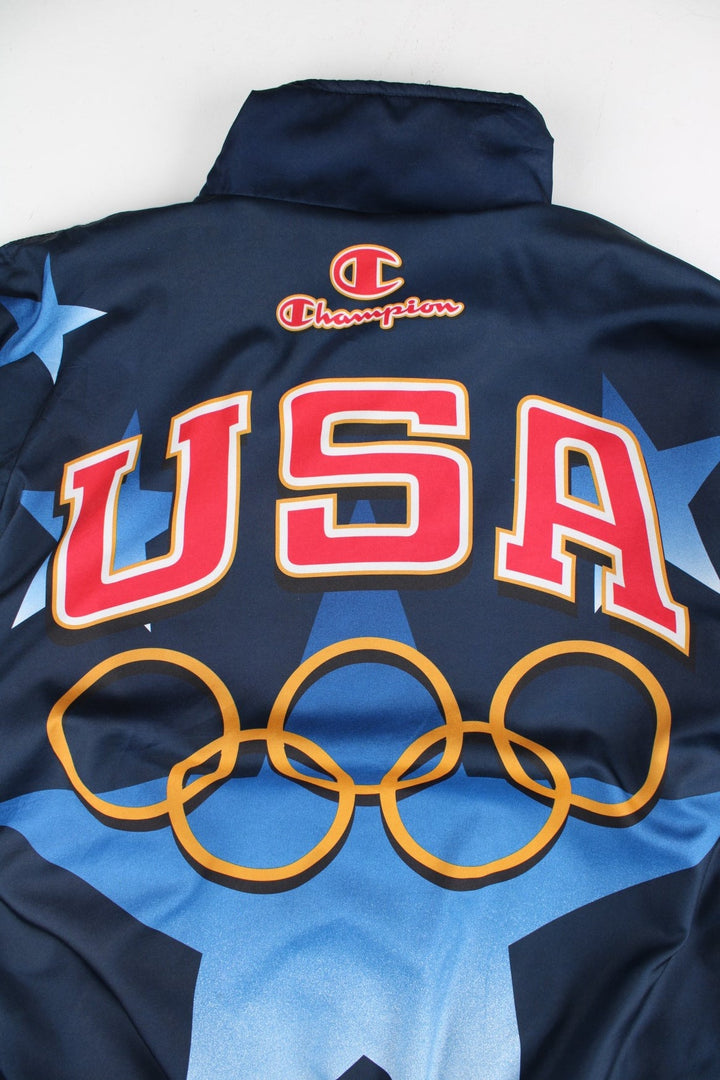 Vintage 1996 Champion USA Olympic Team Track Jacket in a blue colourway. Zips up and has side pockets, and the logos printed on the front, back and on the sleeves.