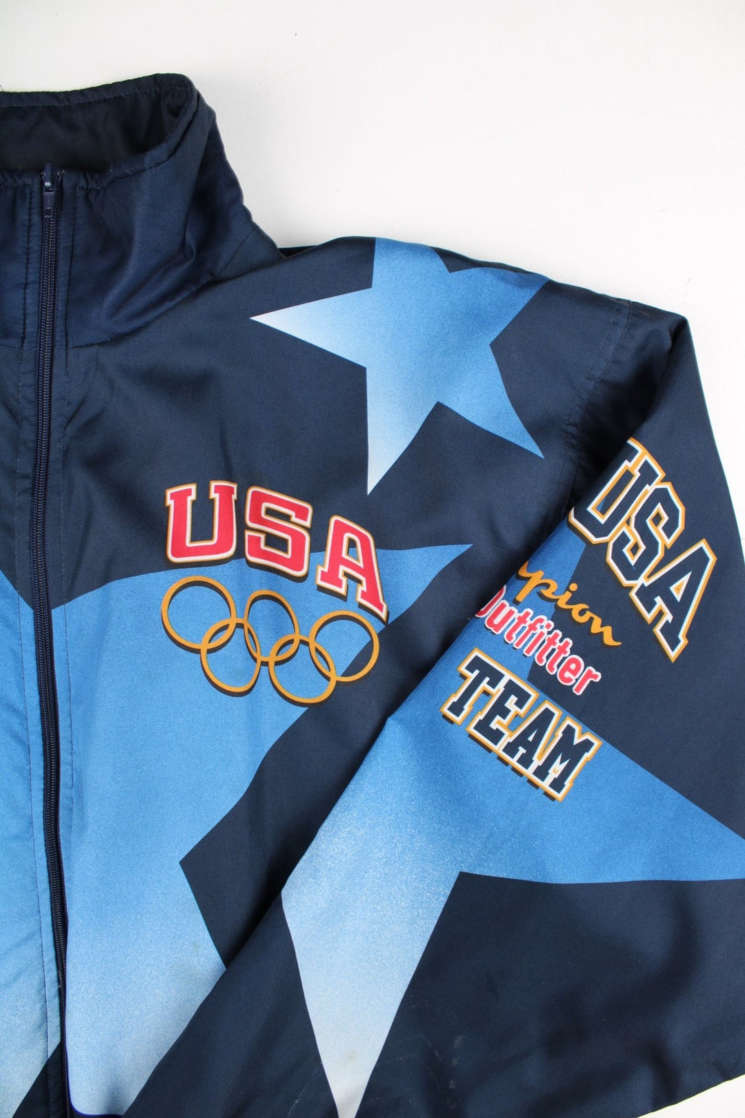 Vintage 1996 Champion USA Olympic Team Track Jacket in a blue colourway. Zips up and has side pockets, and the logos printed on the front, back and on the sleeves.