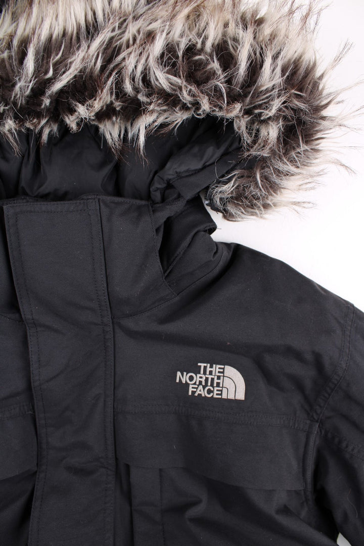 The North Face Parka Coat in a black colourway. Zips up and has multiple pockets, insulated lining, hooded with a detachable faux fur trim, and has the logo embroidered on the front and back.