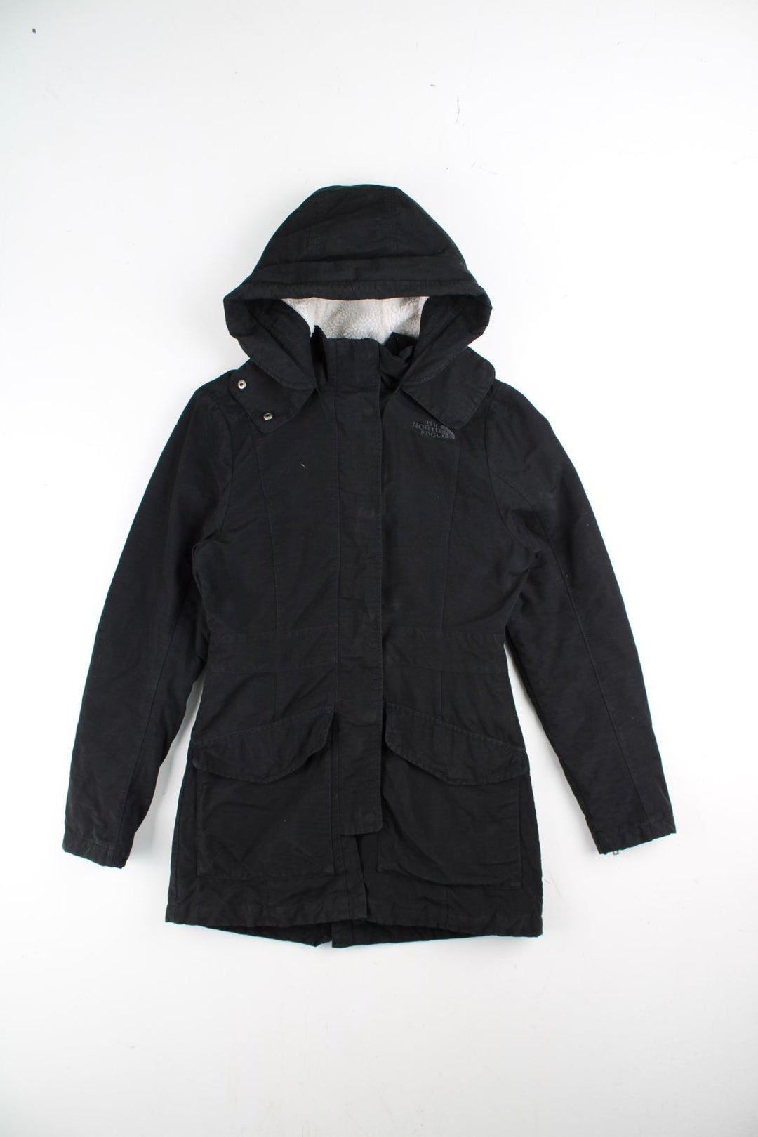 The North Face Parka Coat in a black colourway. Zips and buttons up, has side pockets, insulated with a sherpa lining, hooded, and has the logo embroidered on the front and back.