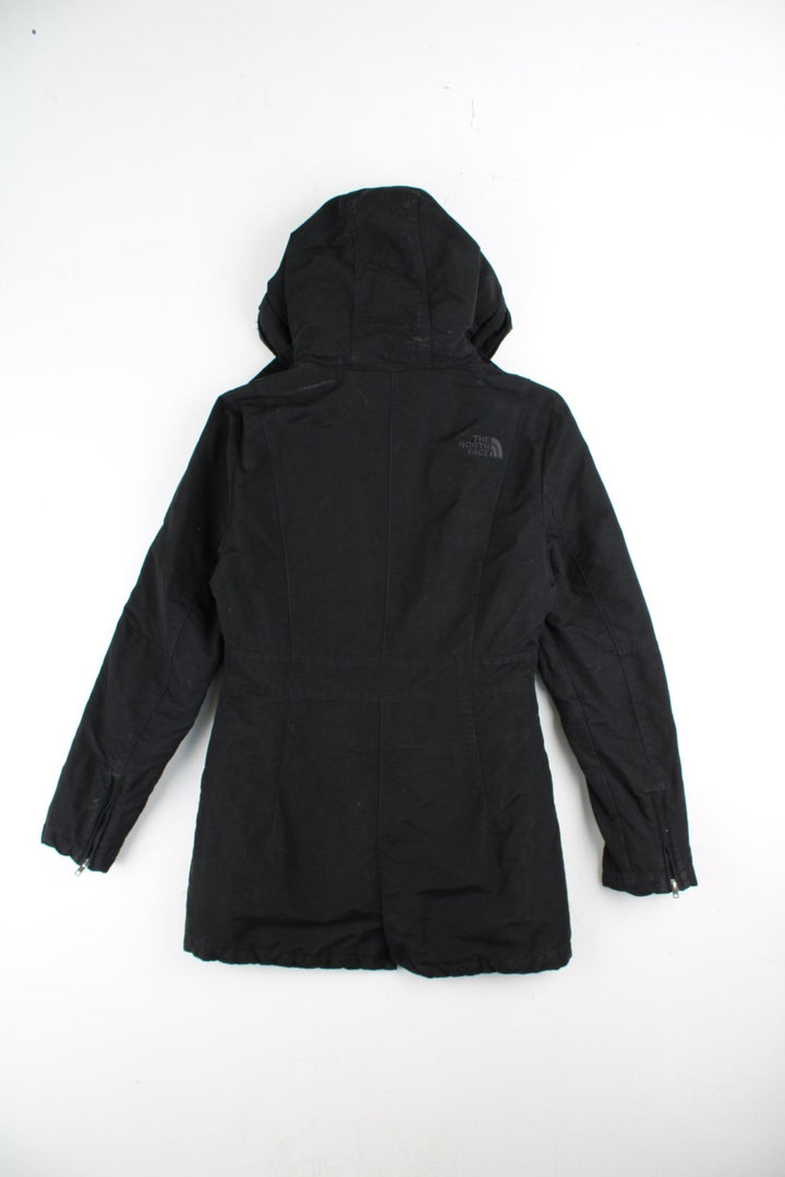 The North Face Parka Coat in a black colourway. Zips and buttons up, has side pockets, insulated with a sherpa lining, hooded, and has the logo embroidered on the front and back.