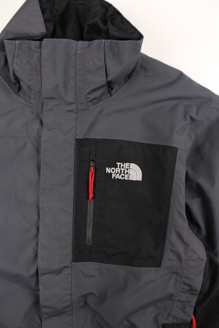 The North Face Jacket in a grey and black colourway. Zips up and has multiple pockets, and the logo embroidered on the front and back.