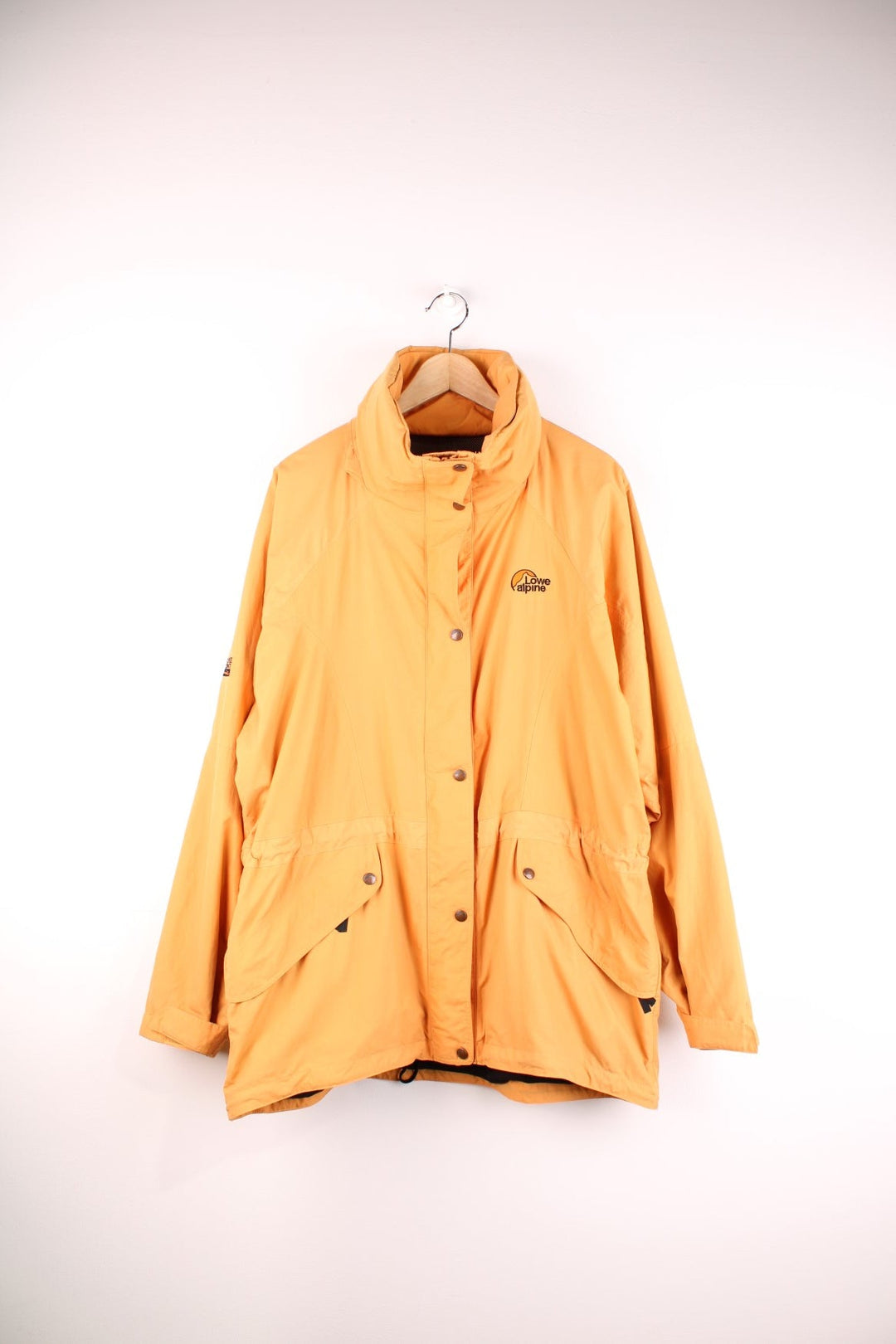 Vintage Lowe Alpine waterproof jacket in yellow with zip and snap closure, two front snapped pockets, an inside pocket, and a retractable hood. 