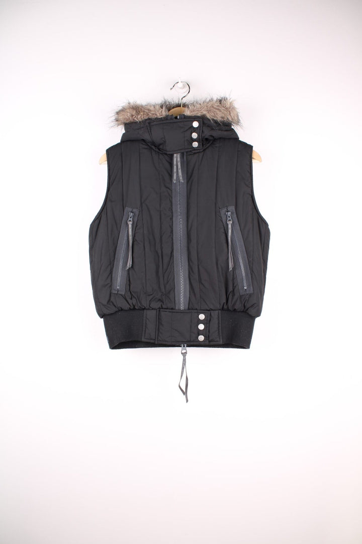  Bench puffa gilet in a black colourway. The gilet has front pockets, with chunky zips, a fur trim hood and is fully lined with grey fleece.