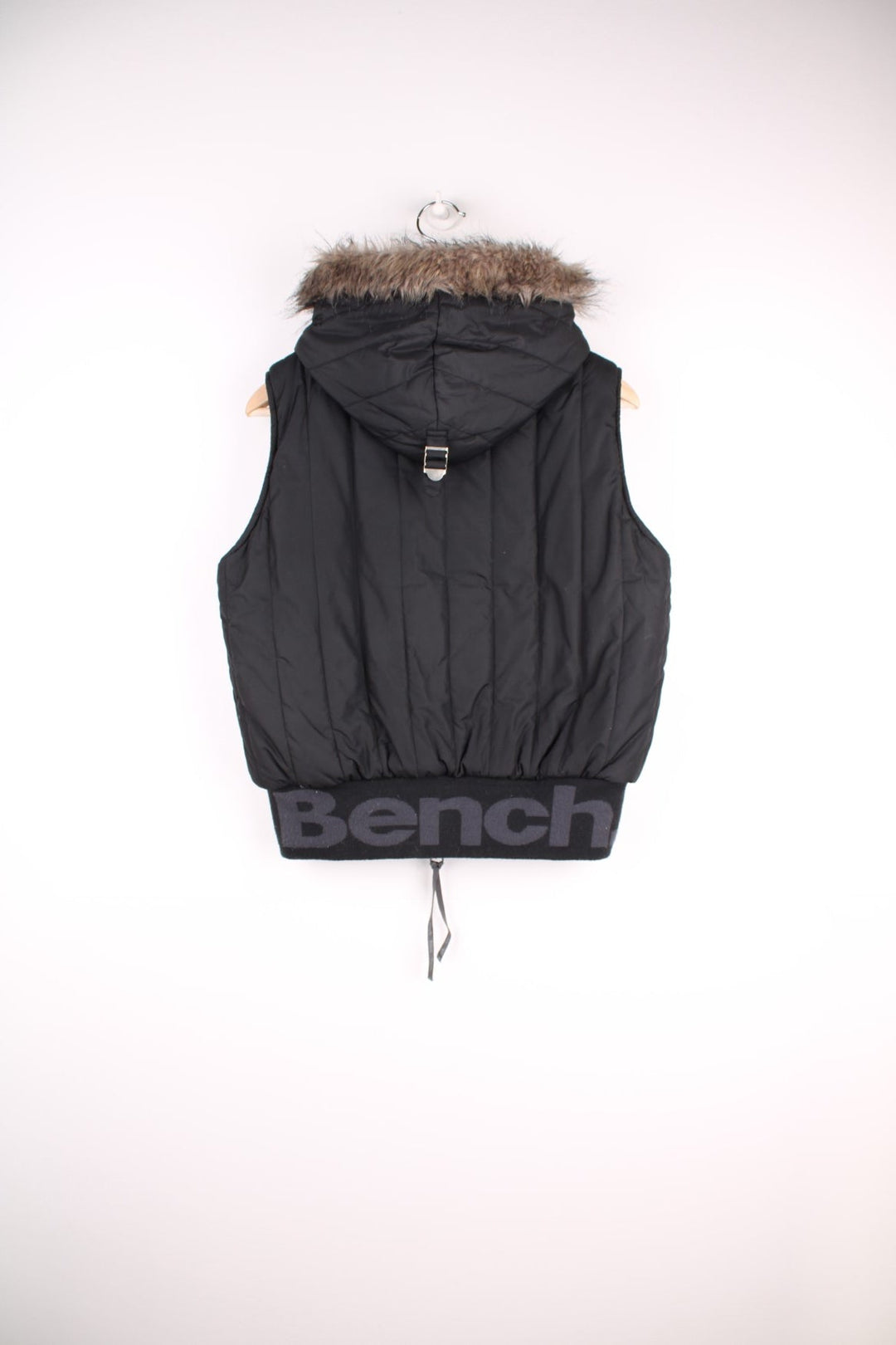  Bench puffa gilet in a black colourway. The gilet has front pockets, with chunky zips, a fur trim hood and is fully lined with grey fleece.