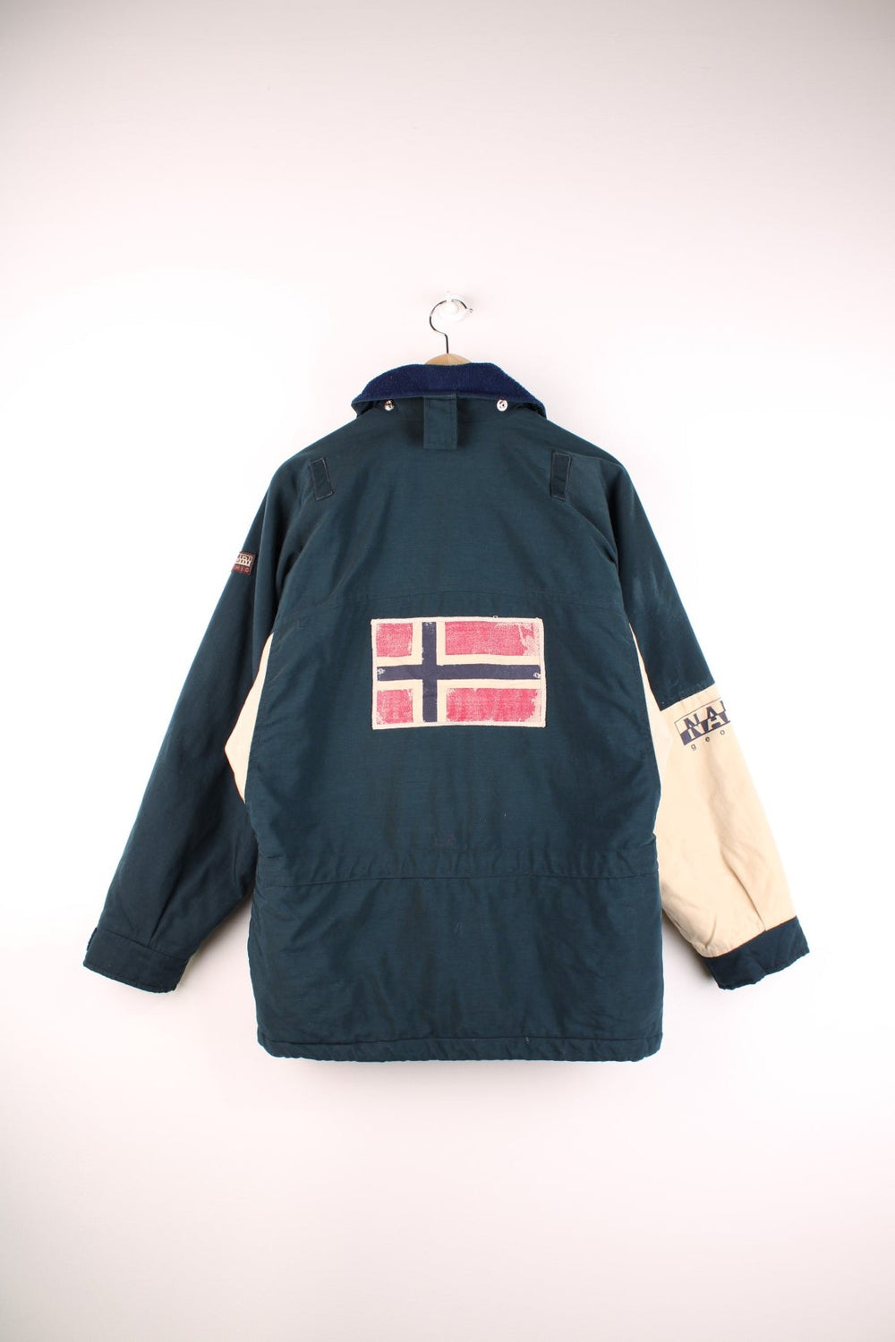 Napapijri Geographic Trans-Antarctica Expedition coat in navy blue and cream with a fleece-lined collar, zip and snap closure, multiple pockets, orange toggles, and patches including a logo on the sleeve and a Norway flag on the back.