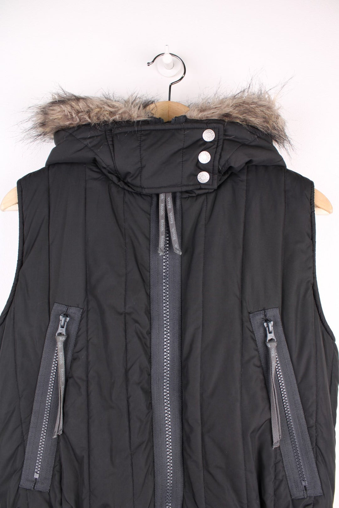  Bench puffa gilet in a black colourway. The gilet has front pockets, with chunky zips, a fur trim hood and is fully lined with grey fleece.